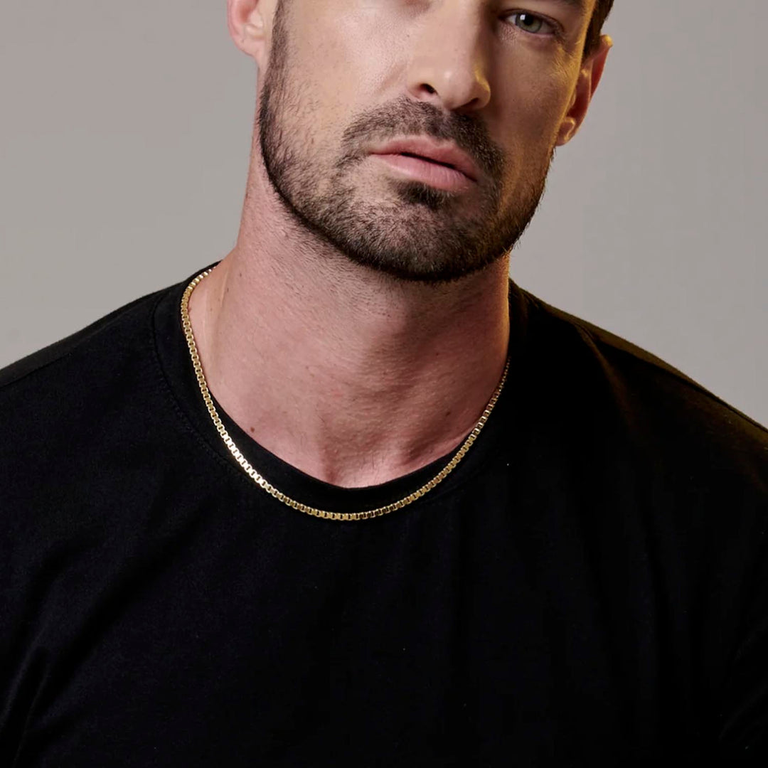 Esta imagen muestra un modelo con una cadena de oro tipo box puesta, que combina perfectamente con una playera negra. La cadena es de alta calidad y tiene un diseño elegante y versátil, lo que la convierte en un accesorio perfecto para cualquier ocasión. La imagen es ideal para aquellos que buscan ver cómo se ve la cadena de oro tipo box puesta en alguien antes de comprarla.