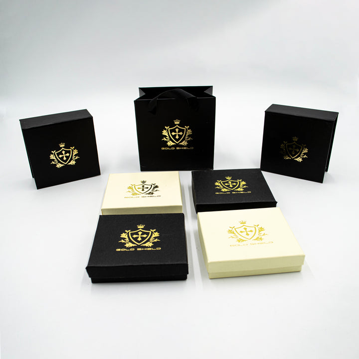 Esta imagen muestra la caja de GoldShield en la que se entrega el dije de cruz de oro 10k con cadena barbada. La caja, de un elegante tono oscuro, garantiza la protección de la joya durante su entrega y aporta un toque extra de lujo a la presentación del producto.